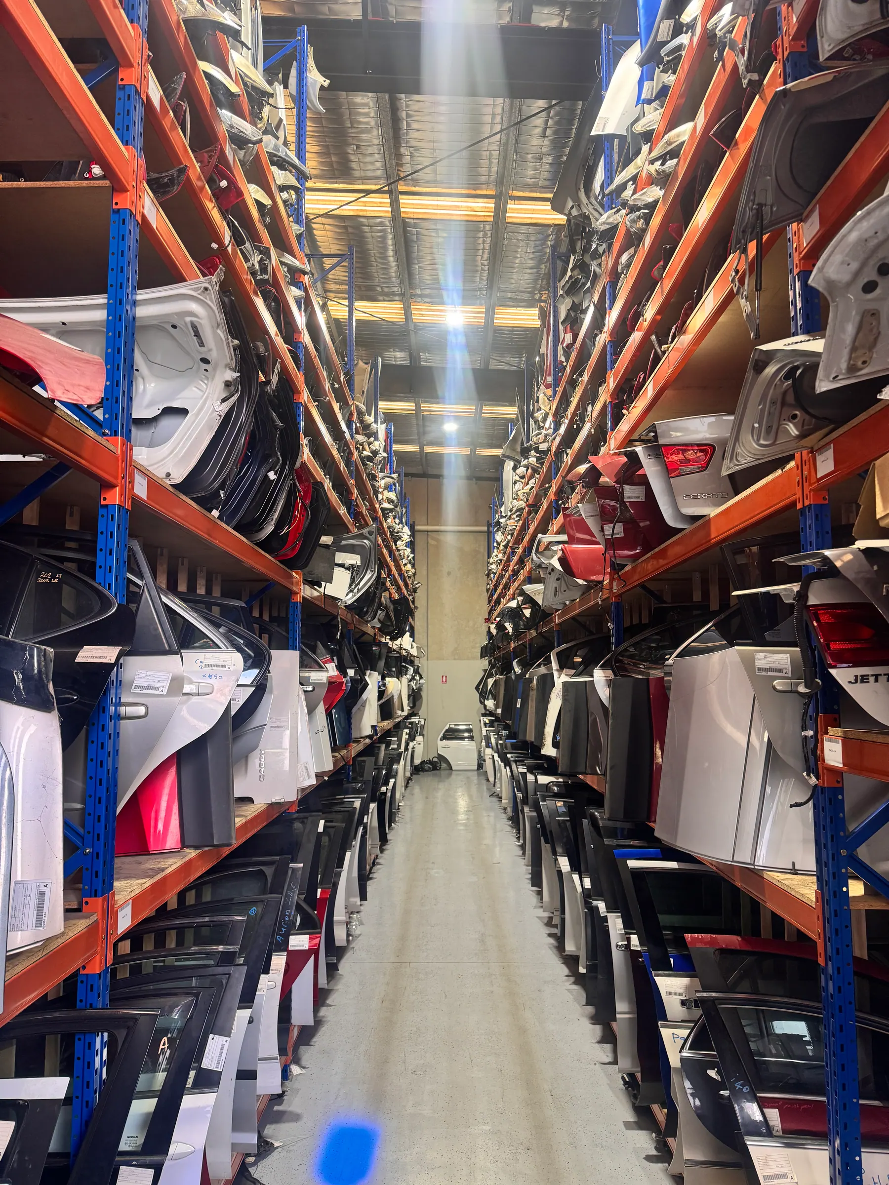 Tall warehouse aisle filled with labelled vehicle panels and parts.
