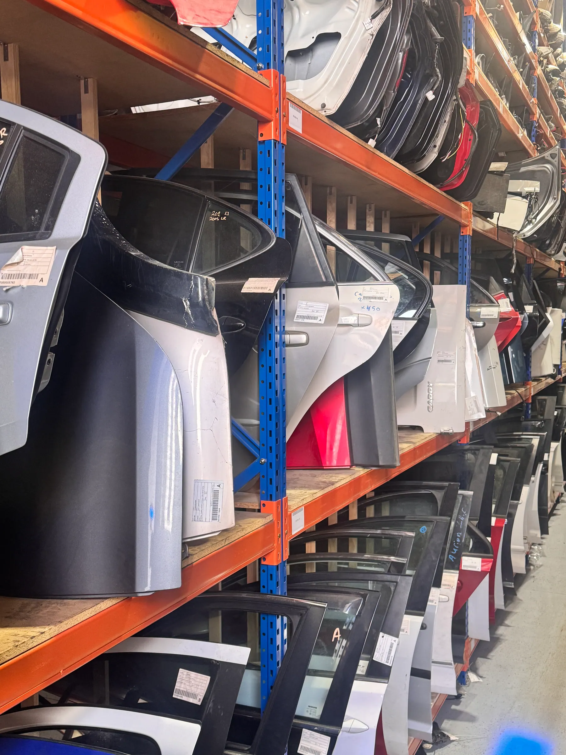 Vehicle doors and body panels stored on orange warehouse racks.
