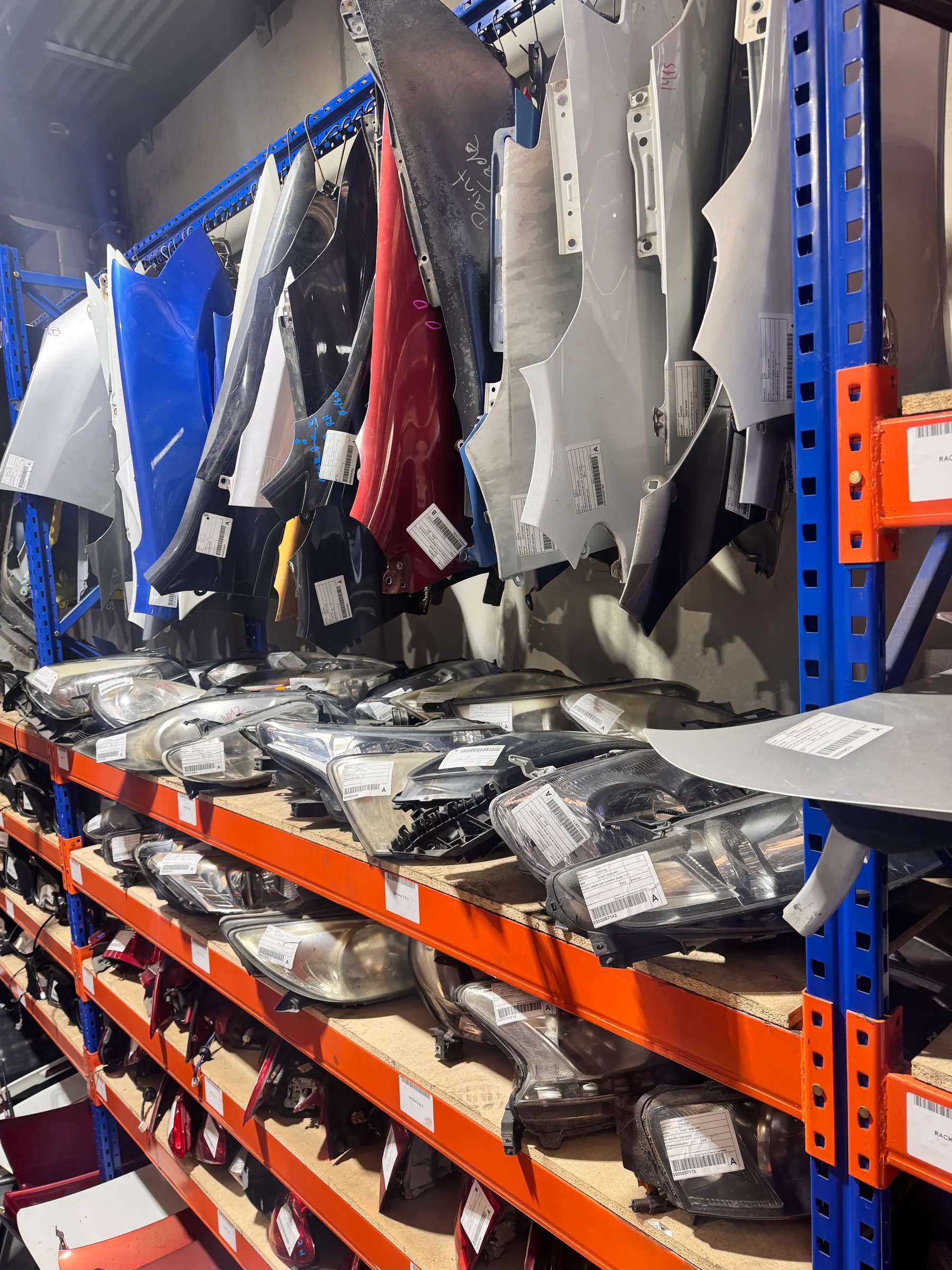 Headlights and body panels organised on PartsBase shelving.