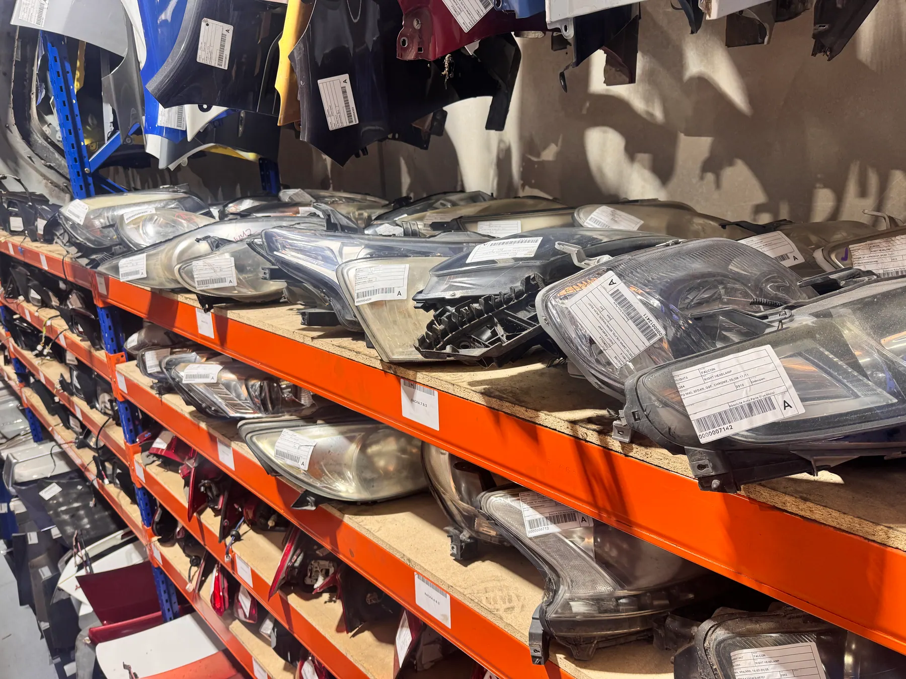 Shelves of labelled vehicle headlights and trim parts.