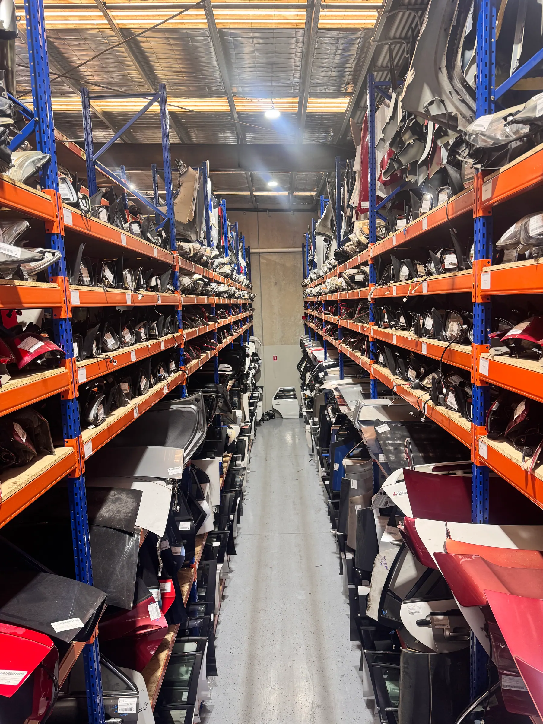 Long warehouse aisle with dismantled vehicle parts on both sides.