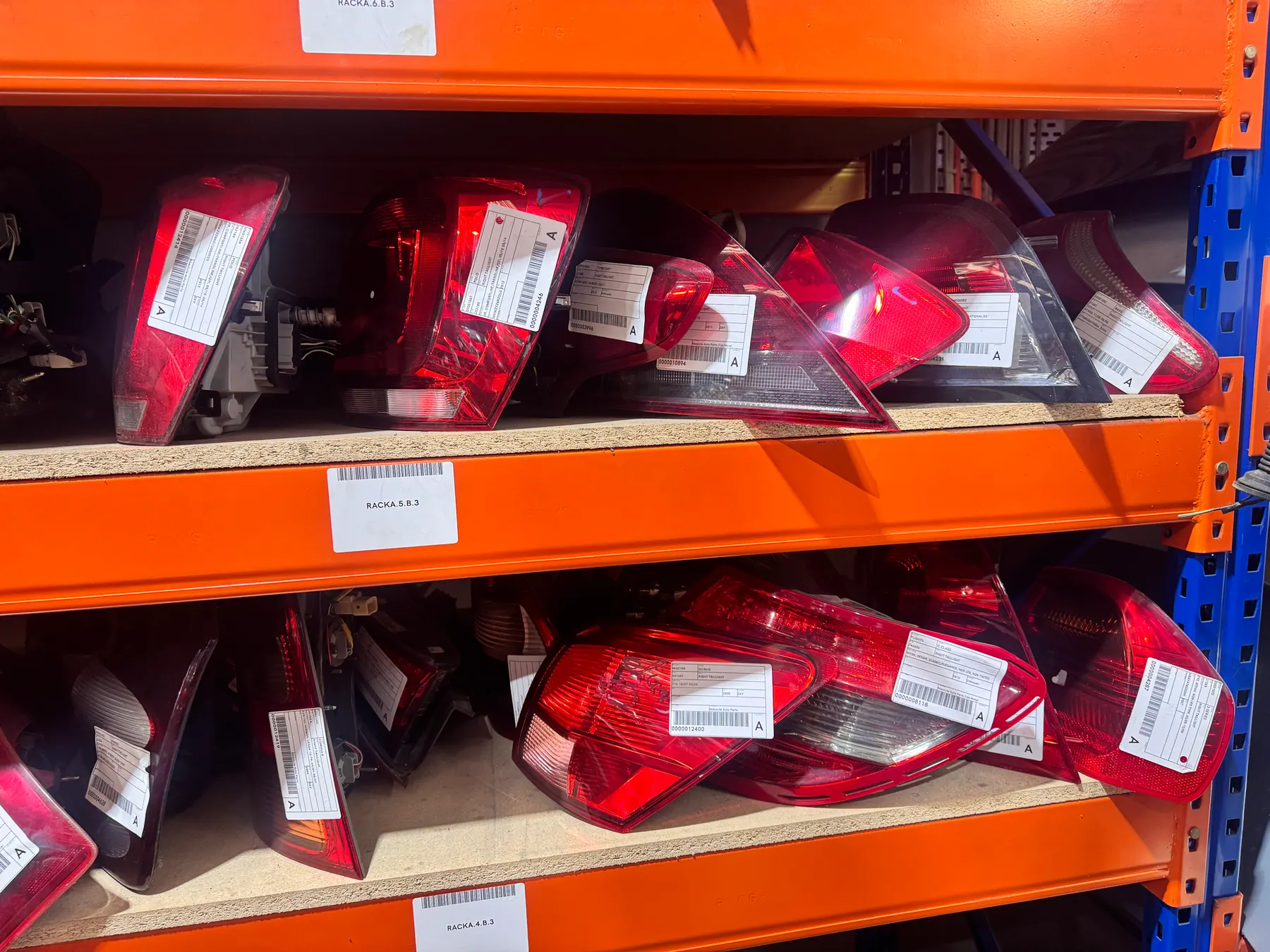 Red tail lights with stock labels on orange warehouse shelving.