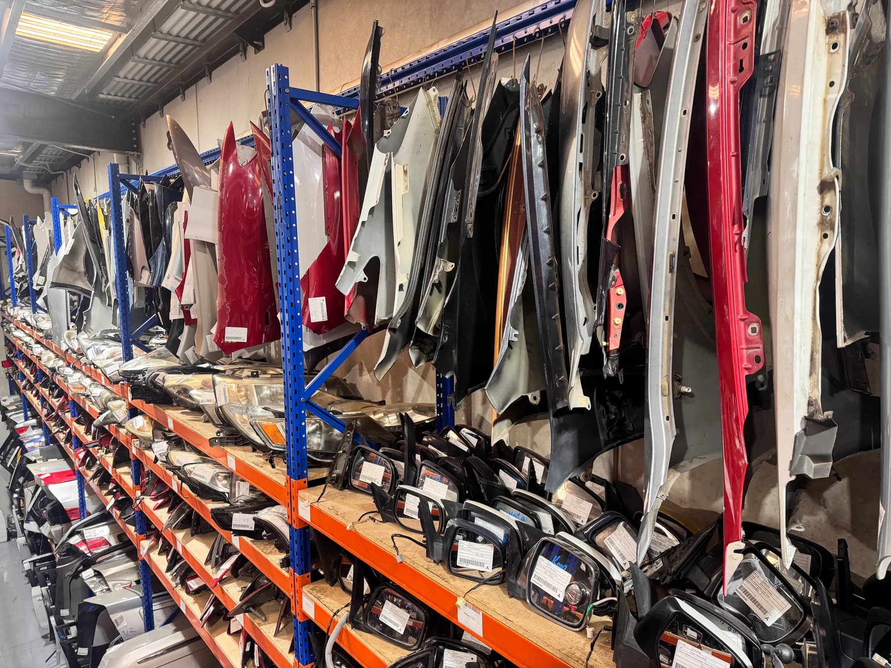 Vehicle doors and panels arranged along tall storage racks.