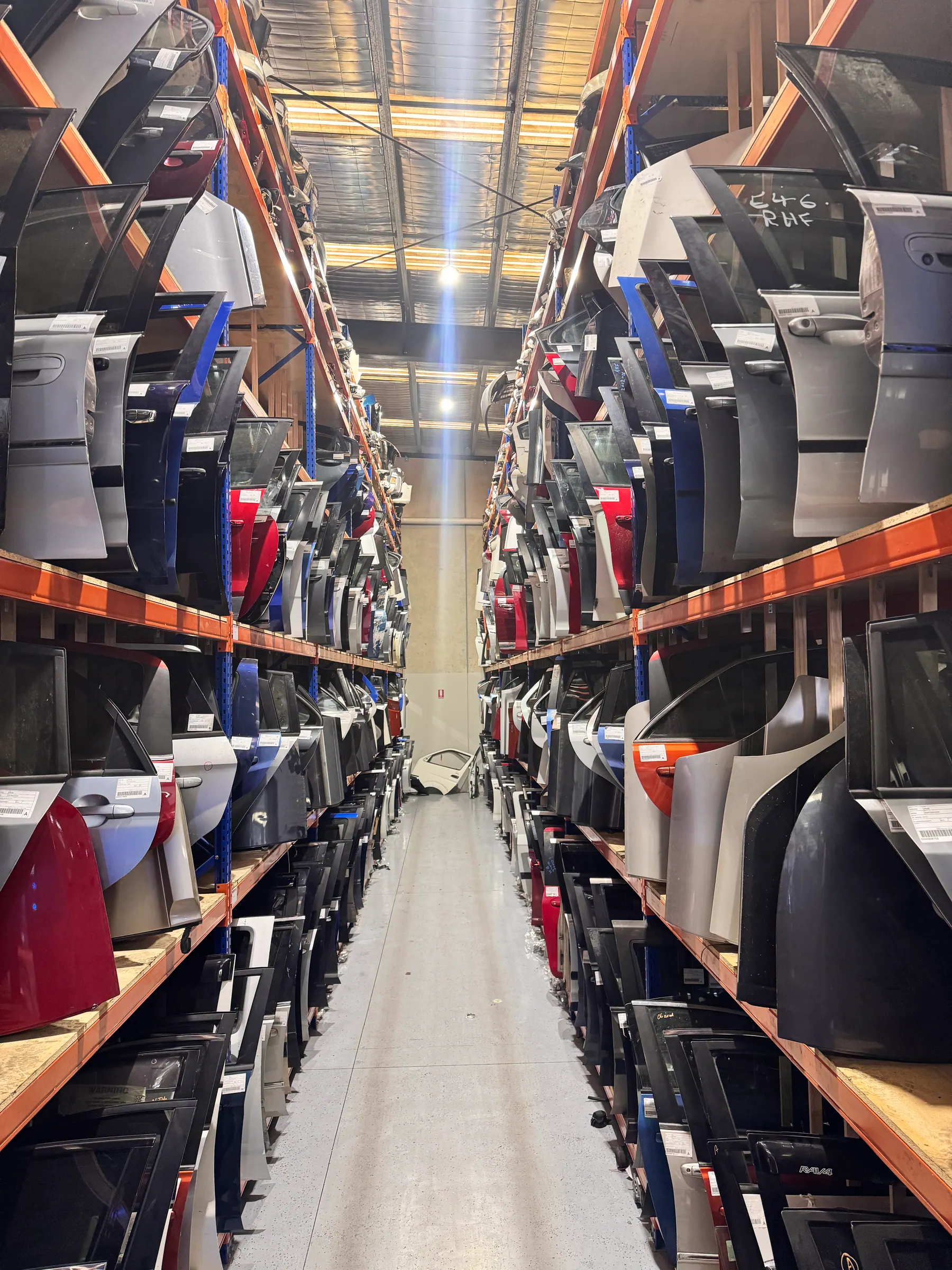 Deep aisle of vehicle doors and panels inside the PartsBase warehouse.