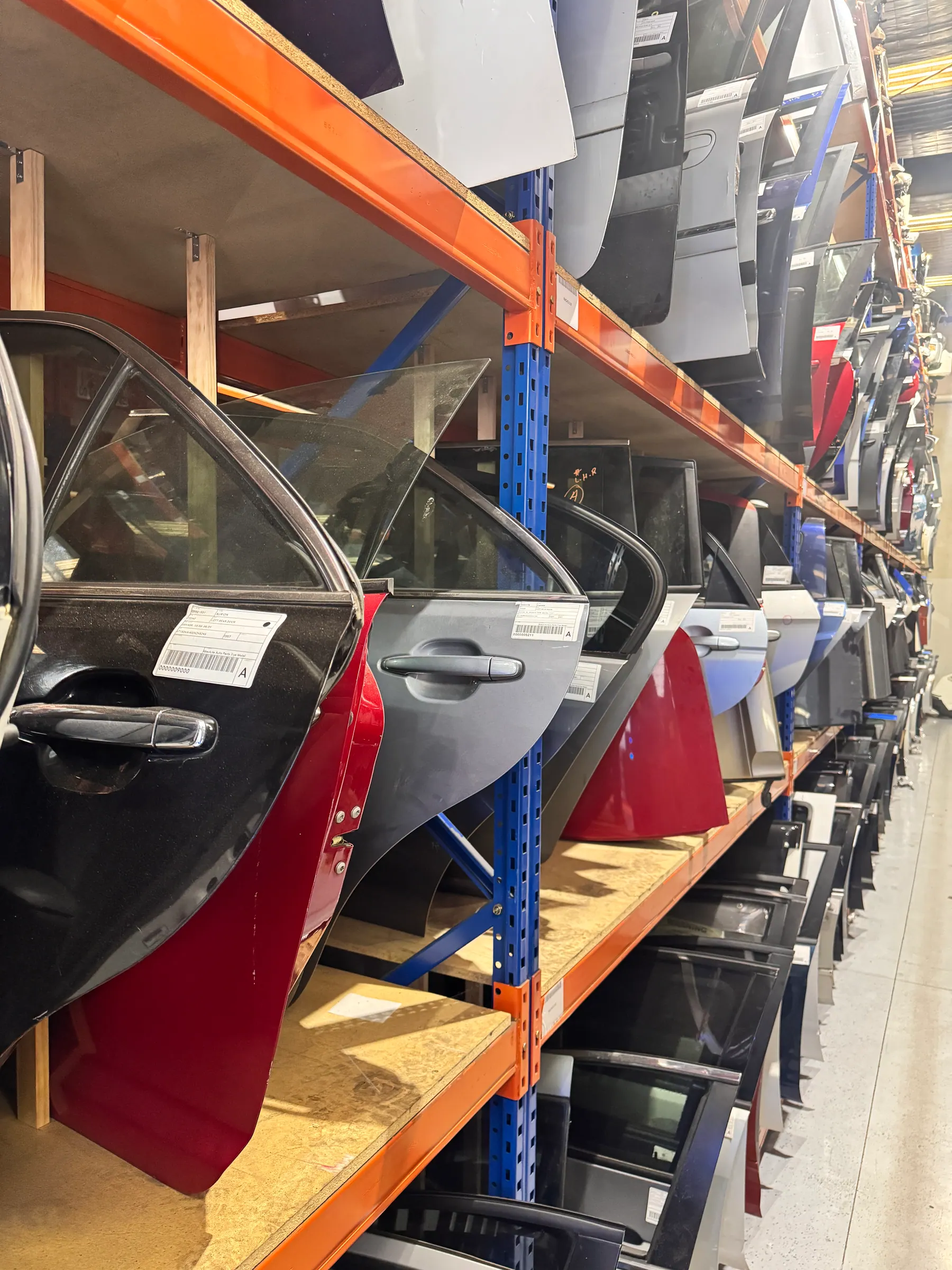 Red and grey vehicle doors stored vertically on warehouse shelving.