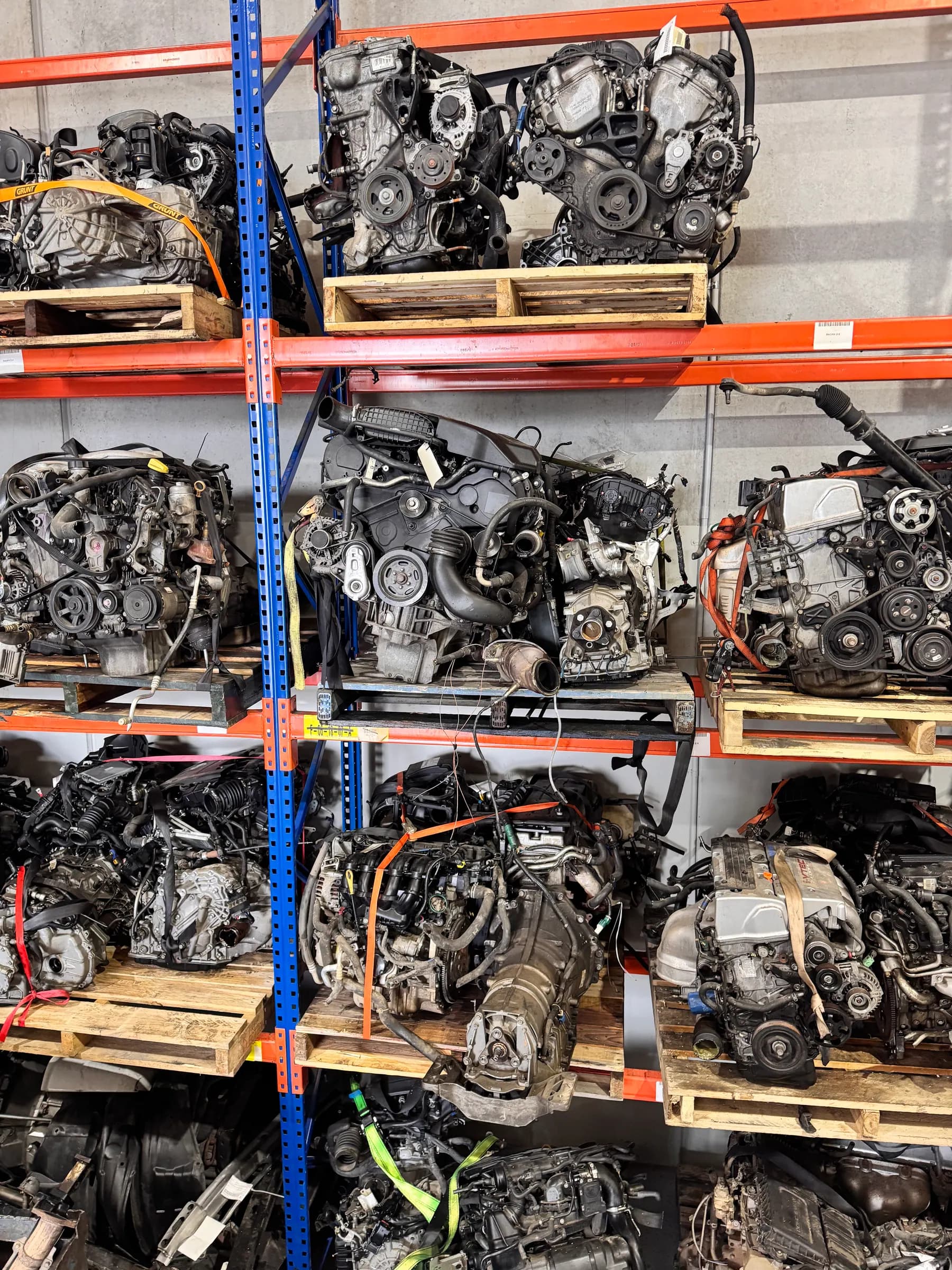 Multiple used engines organised on blue and orange warehouse racks.