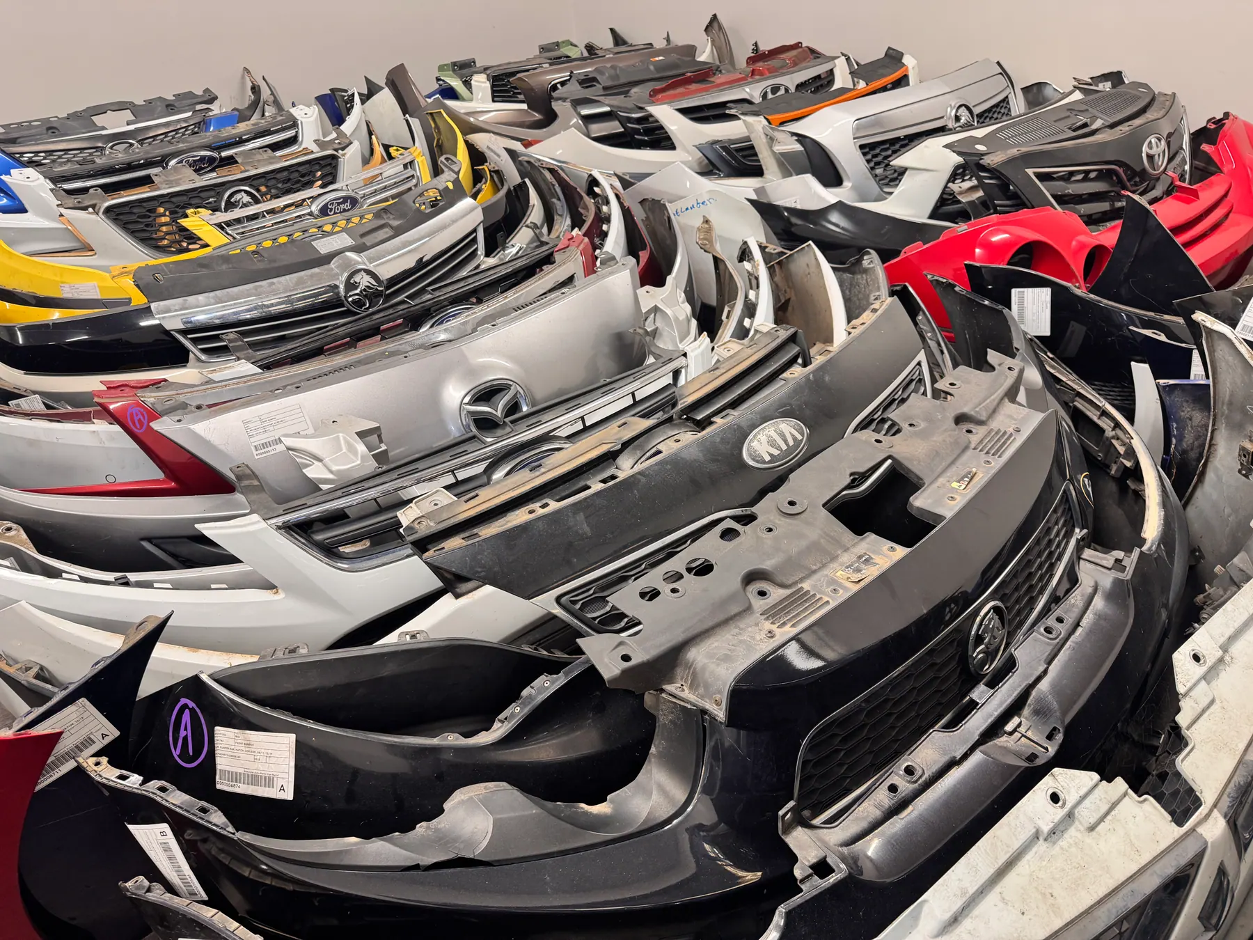 Rows of vehicle bumpers and grilles grouped by make and model.